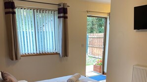 A neatly made bed with two pillows, a wooden nightstand with a patterned item, and a window with blinds. - Rooms at the Huntsman Inn (Falfield)