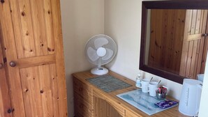 A wooden wardrobe, a wooden desk with a white fan, a mirror, and a coffee maker. - Rooms at the Huntsman Inn (Falfield)