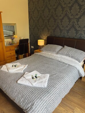 A neatly made bed with a patterned bedspread, a bedside table with a lamp, and a dresser with a mirror. - Rooms at the Huntsman Inn (Falfield)