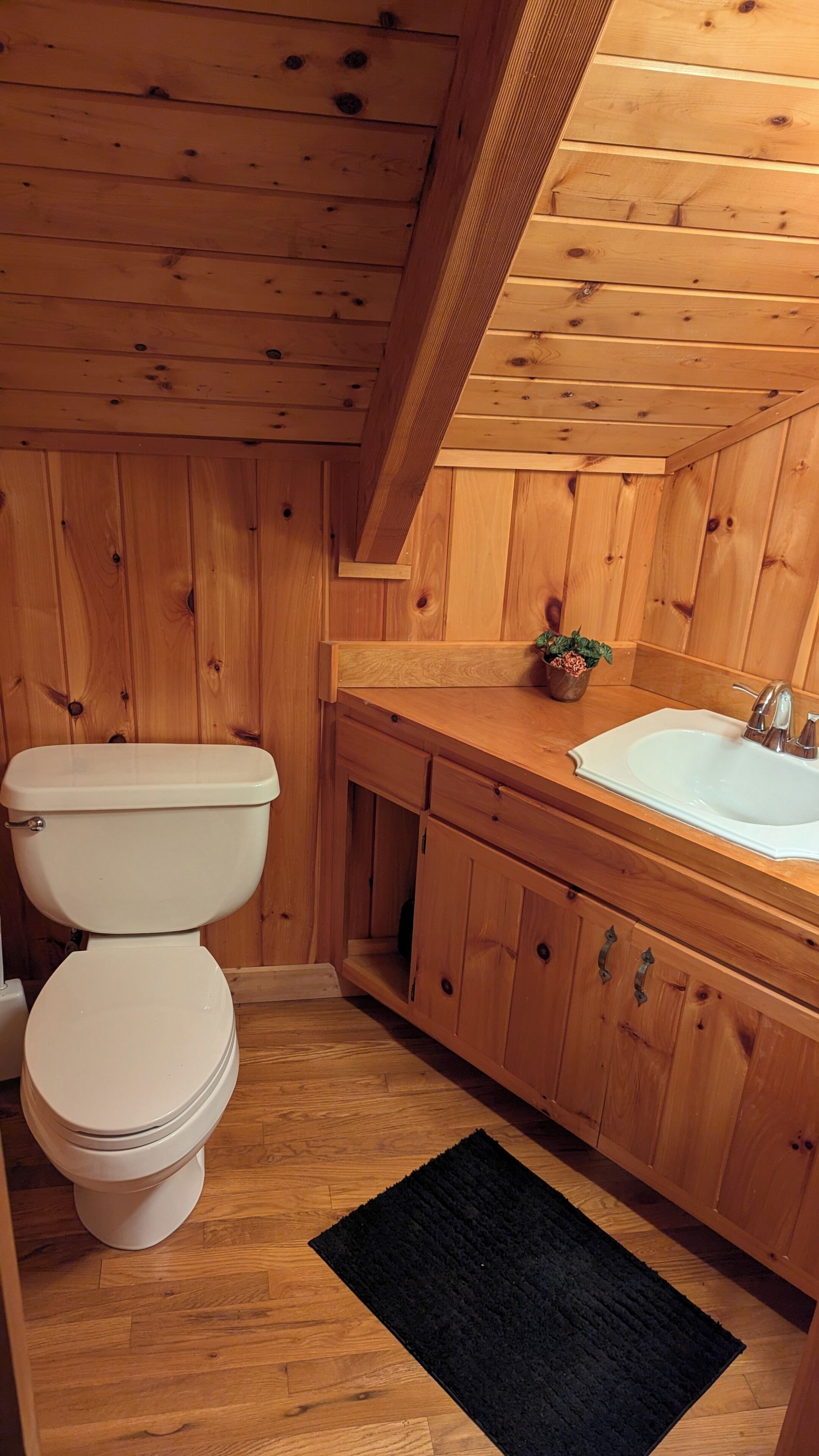 A wooden bathroom with a toilet, sink, and cabinets.