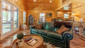 A cozy cabin interior with a green leather sofa, wooden flooring, and a dining area with a rustic kitchen. - Brand New! Hickory Wind: Charming 2 Bedroom Cabin in Whittier (Whittier)