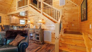 A cozy cabin interior with a wooden staircase, a fireplace, a leather sofa, and a rustic dining area. - Brand New! Hickory Wind: Charming 2 Bedroom Cabin in Whittier (Whittier)