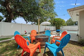A backyard with a fire pit, outdoor chairs, and a grill.