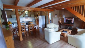A spacious living area with a wooden staircase, a dining table with chairs, a sofa, and a television.