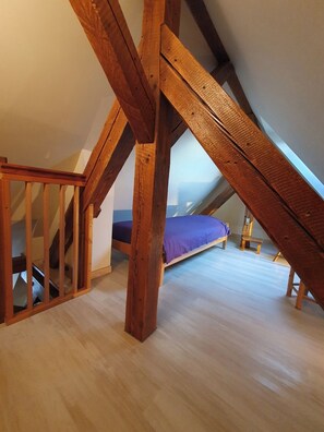 An attic bedroom with a sloped ceiling, wooden beams, a bed with a blue mattress, and a small wooden chair. - Vacation rental for 5 people in Alsace (Aspach-le-Bas)