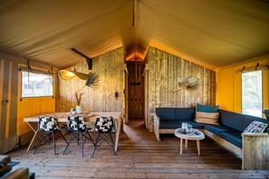 A wooden interior with a dining area, sofa, and a small table with chairs. - Safari Tent in Markelo Near Nature Park (Markelo)