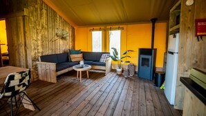 Un interior de cabaña acogedor con suelo de madera, un sofá, una mesa de comedor y una pequeña cocina con estufa.