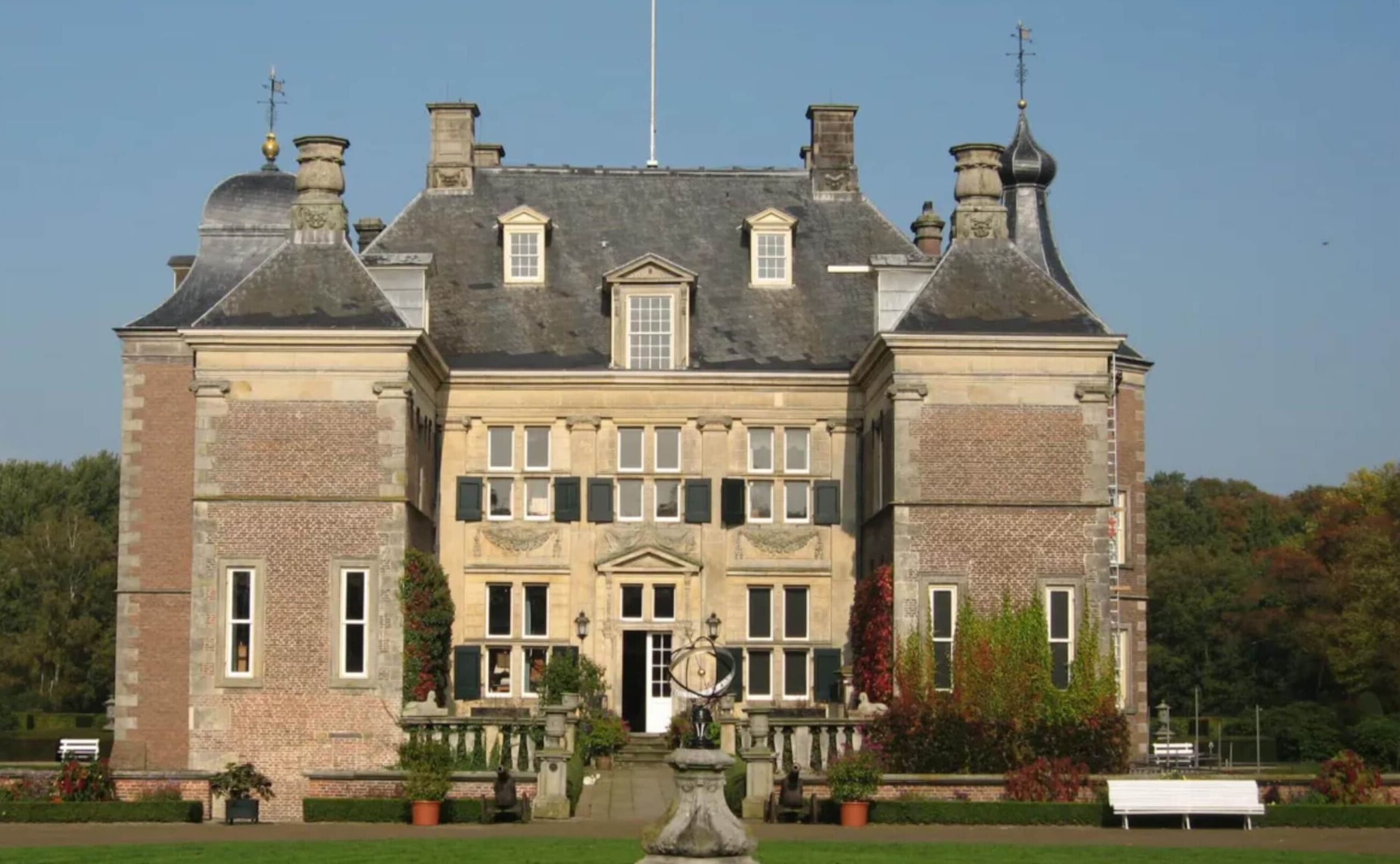 Un edificio grande e histórico con una fachada simétrica, múltiples chimeneas y una entrada central con una reja decorativa.