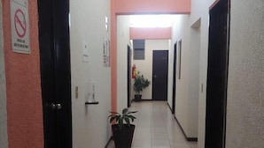 A hallway with doors on both sides, a potted plant in the center, and a sign on the floor indicating social distancing. - HOTEL HUMBERTO (Tepic)