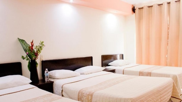 A hotel room with three beds, a nightstand with a water bottle, and a decorative plant. - HOTEL HUMBERTO (Tepic)