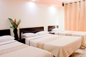 A hotel room with three beds, a nightstand with a water bottle, and a decorative plant.