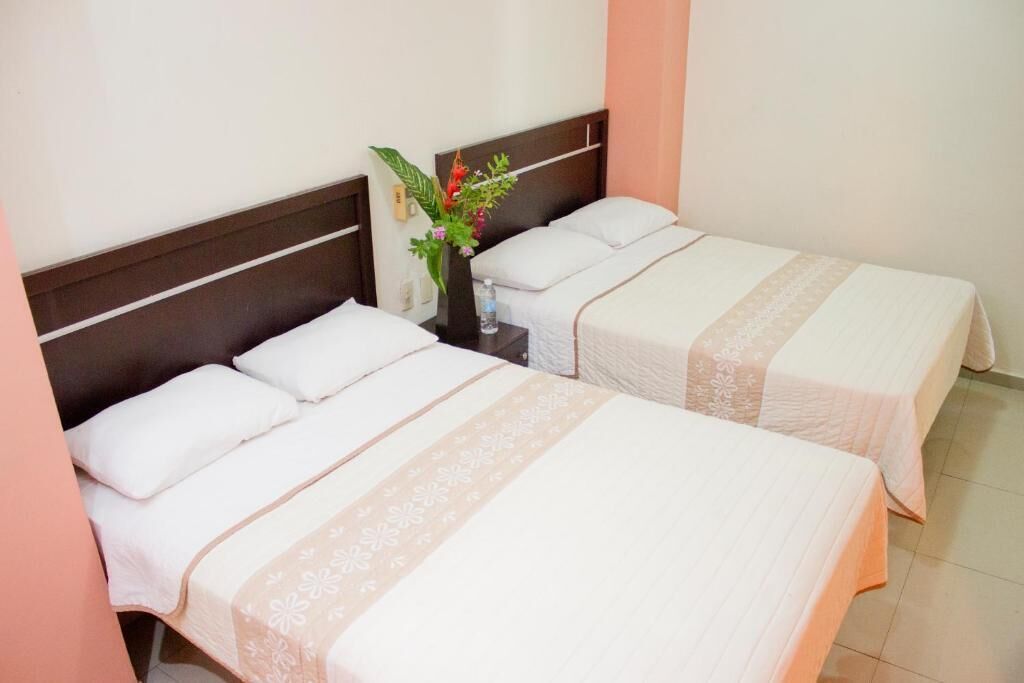 Two single beds with white linens and floral patterns, a nightstand with a vase of flowers, and a wooden headboard.