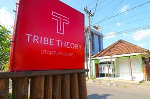 A red sign with the text "TRIBE THEORY STARTUP HOUSE" and a building in the background.