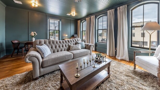 Un salon avec un canapé capitonné, une table basse en bois ornée de bougies et un ventilateur de plafond.