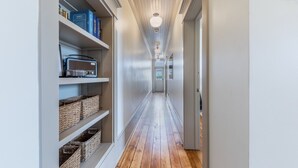 Un couloir étroit au plancher en bois, aux murs blancs, et dont l’étagère, située sur le côté gauche, est garnie de paniers et de livres.