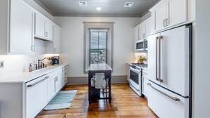 Une cuisine moderne avec des meubles blancs, un îlot central, un four à micro-ondes, un réfrigérateur et une fenêtre donnant sur un beau paysage.