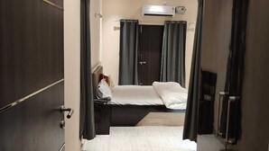 A hotel room with a bed, a bedside table, an air conditioning unit, and a wardrobe.
