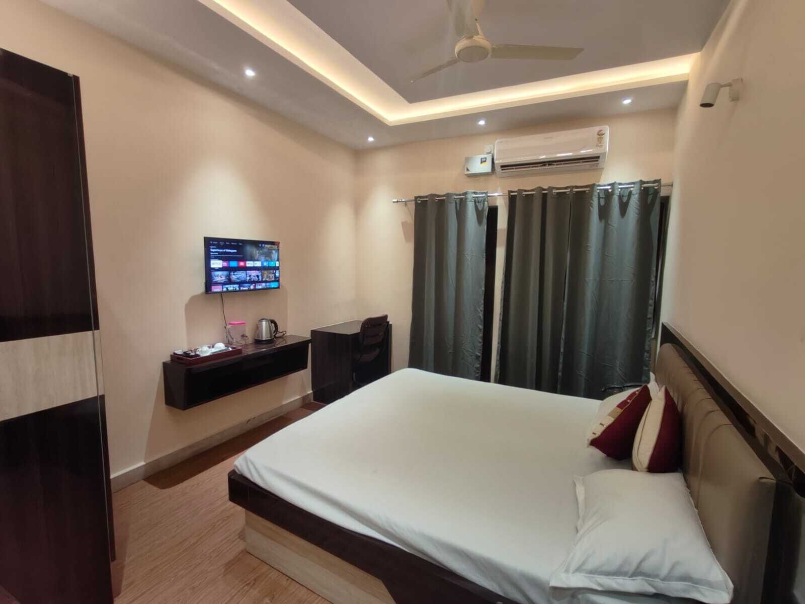 A hotel room with a bed, a TV, a desk, and an air conditioning unit.