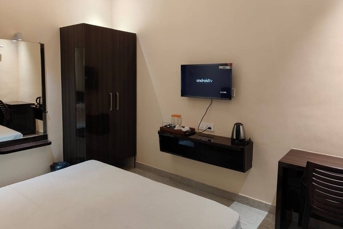 A hotel room with a bed, a wardrobe, a TV mounted on the wall, and a small table with a coffee machine.
