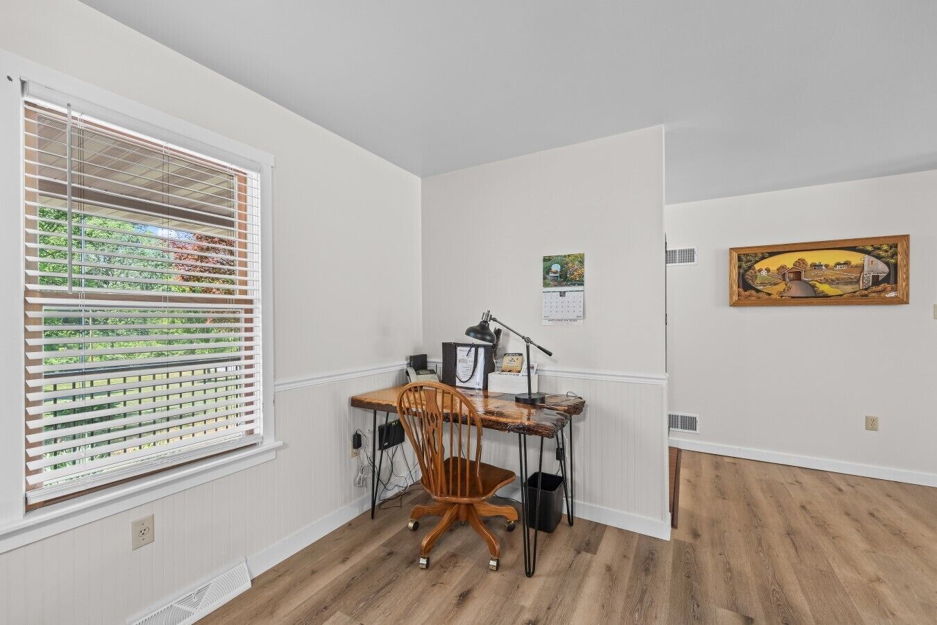 A room with a wooden desk, chair, and a window with blinds.