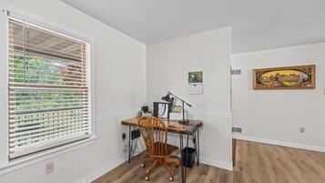 A room with a wooden desk, chair, and a window with blinds.