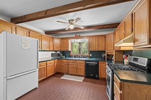A kitchen with wooden cabinets, a white refrigerator, a microwave, a stove, and a ceiling fan.