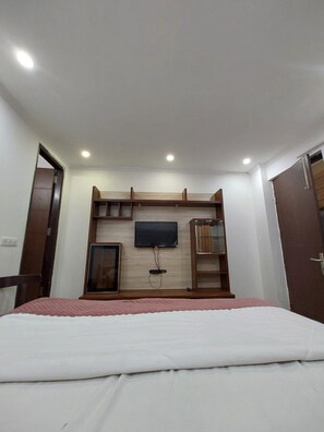 A bedroom with a bed, a TV mounted on the wall, and a built-in shelf. - Vinayak Stay Sector 43 (Gurugram)