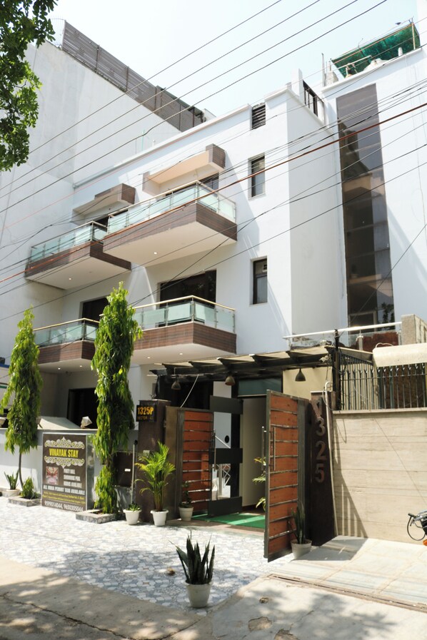 A modern building with multiple balconies, potted plants, and a sign indicating a business establishment. - Vinayak Stay Sector 43 (Gurugram)
