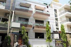A multi-story building with balconies, a signboard advertising amenities, and a parked scooter. - Vinayak Stay Sector 43 (Gurugram)
