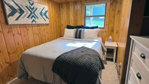 Une chambre à coucher aux murs lambrés, avec un lit, des oreillers, une table de chevet, une commode et une fenêtre.