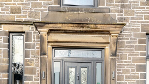 A stone building with a dark grey door, a window with a glass door, and a sign above the door that reads "MOAT HOUSE". - Moat House Room 5|Private Bathroom (Rossendale)