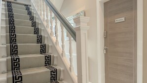 A staircase with a patterned carpet, white balusters, and a wooden door with a nameplate. - Moat House Room 5|Private Bathroom (Rossendale)