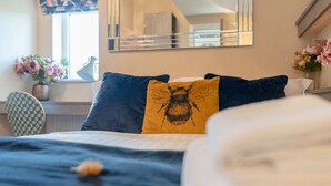 A bed with a blue and yellow pillow, a vase with flowers, and a mirror on the wall. - Moat House Room 5|Private Bathroom (Rossendale)