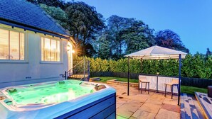 A hot tub in a backyard with a covered patio area and a staircase leading to a house.