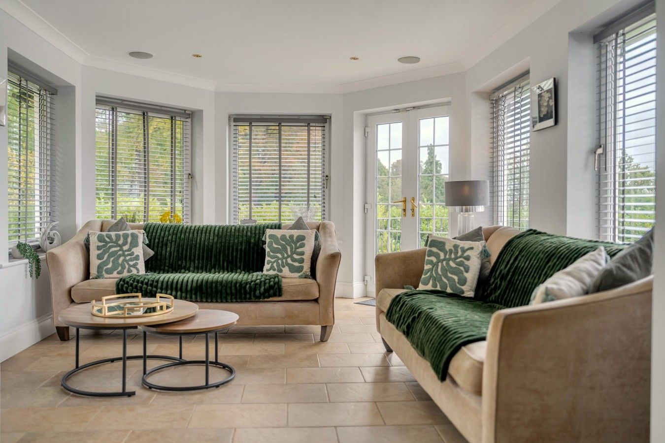 A spacious living room with two sofas, a coffee table, and large windows with blinds.