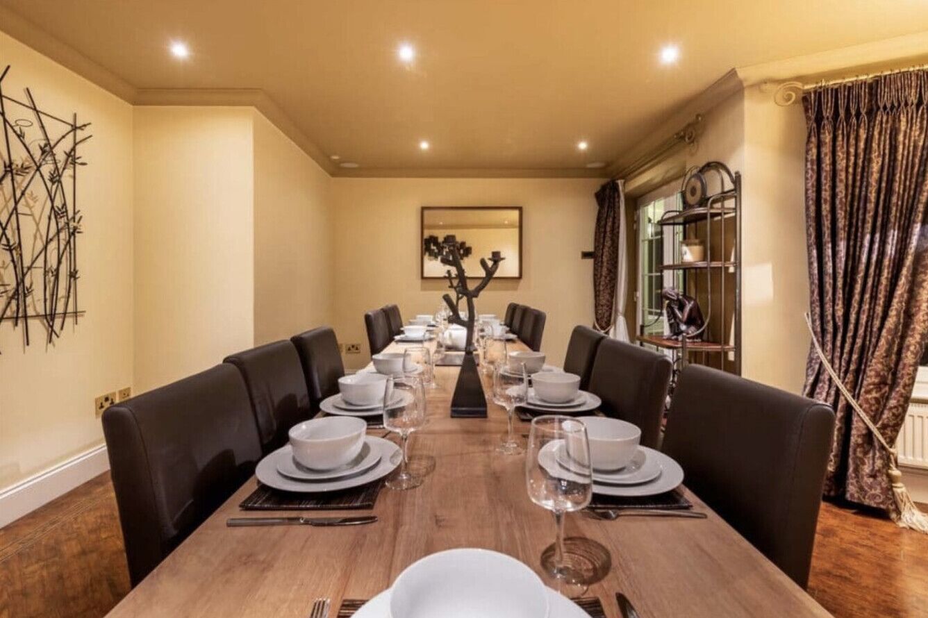 Une salle à manger élégante, avec une longue table dressée pour un repas, entourée de fauteuils en cuir foncé.