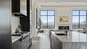 A modern kitchen with a large island, dark cabinetry, and a view of mountains through large windows. - Zion Mountain / Pool, Hot Tub, BBQ & Pickleball (Washington)