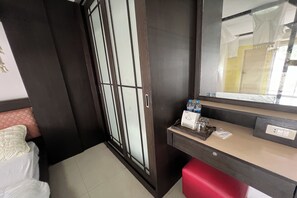 A hotel room with a bed, a wardrobe, a mirror, a small table with toiletries, and a red storage box. - Pongsatorn Mansion by Zuzu (Bangkok)