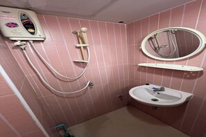 A bathroom with pink tiled walls, a white pedestal sink, a handheld showerhead, and a wall-mounted mirror. - Pongsatorn Mansion by Zuzu (Bangkok)