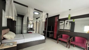A modern hotel room with a bed, two red chairs, a desk with a telephone, and a TV. - Pongsatorn Mansion by Zuzu (Bangkok)