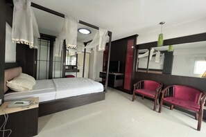 A modern hotel room with a bed, two red chairs, a desk with a telephone, and a TV. - Pongsatorn Mansion by Zuzu (Bangkok)