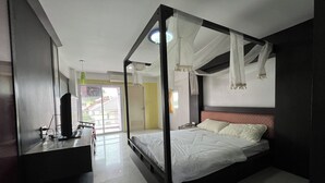 A bedroom with a four-poster bed, a desk with a computer, and a view of the outside. - Pongsatorn Mansion by Zuzu (Bangkok)