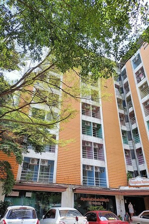 Un edificio de varios pisos con una combinación de paredes exteriores de ladrillo y blanco, unidades de aire acondicionado en las ventanas, y un letrero que indica un negocio o servicio en la planta baja.