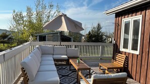 Een houten terras met een witte reling, een beige parasol, een witte hoekbank en houten stoelen.