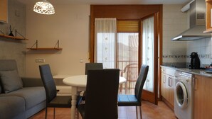 A compact kitchen with a washing machine, a dining table with chairs, and a sofa.