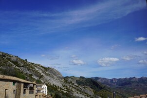 Paisaje montañoso con edificios de piedra tradicionales, cielo despejado y montañas distantes.