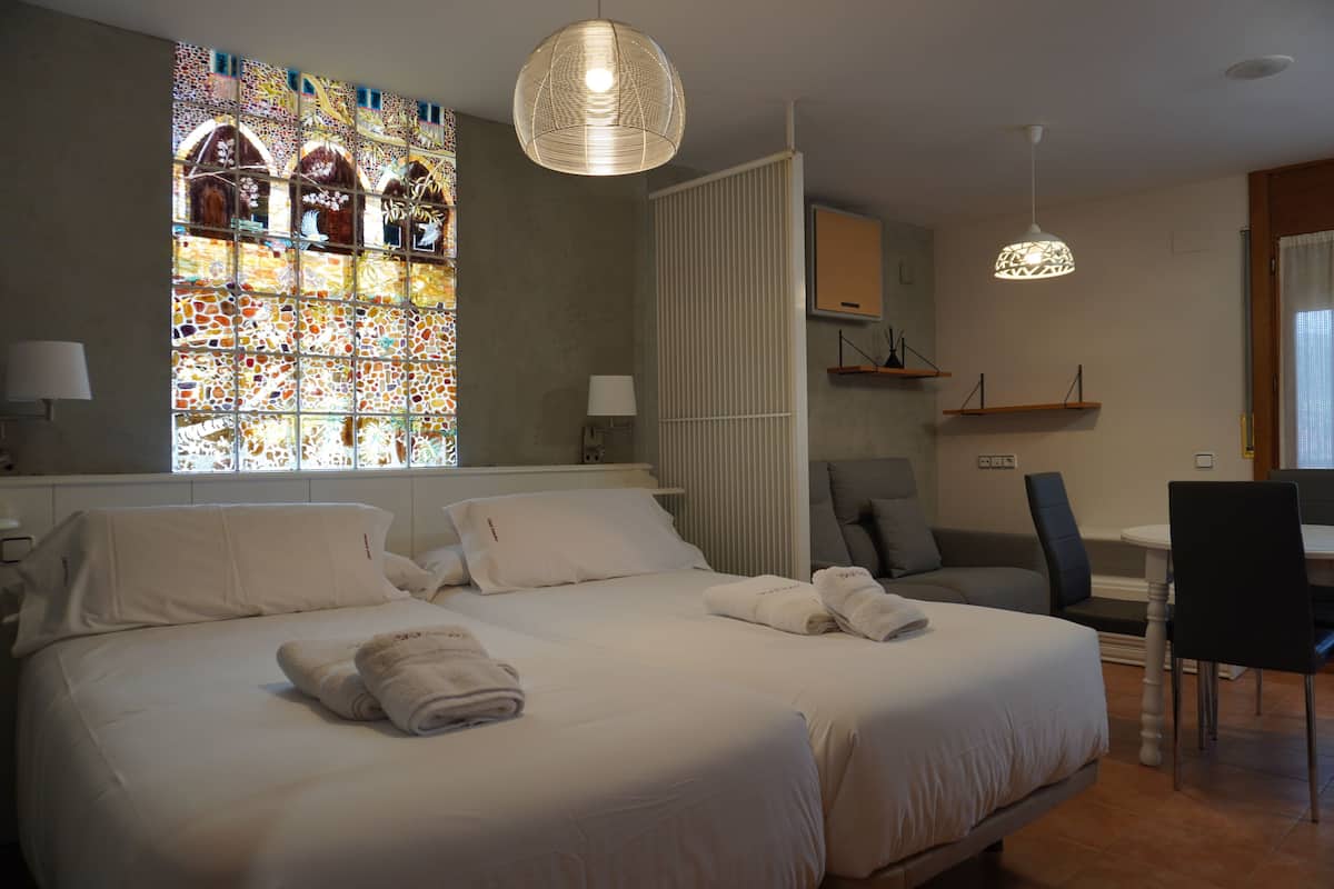 Et hotelværelse med en stor seng, spiseplads, et vindue med farvet glas og en hængende lampe.