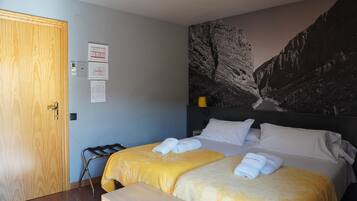 Une chambre d’hôtel avec deux lits, une porte en bois, un luminaire fixé au mur et une fresque représentant une montagne.