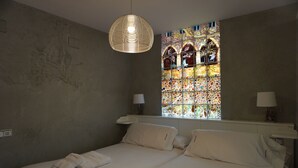 A bedroom with two beds, a large stained glass window, and a hanging light fixture.