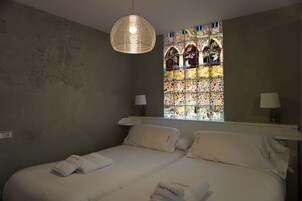 Un dormitorio con dos camas, un amplio ventanal con vidrieras de colores y una lámpara colgante.